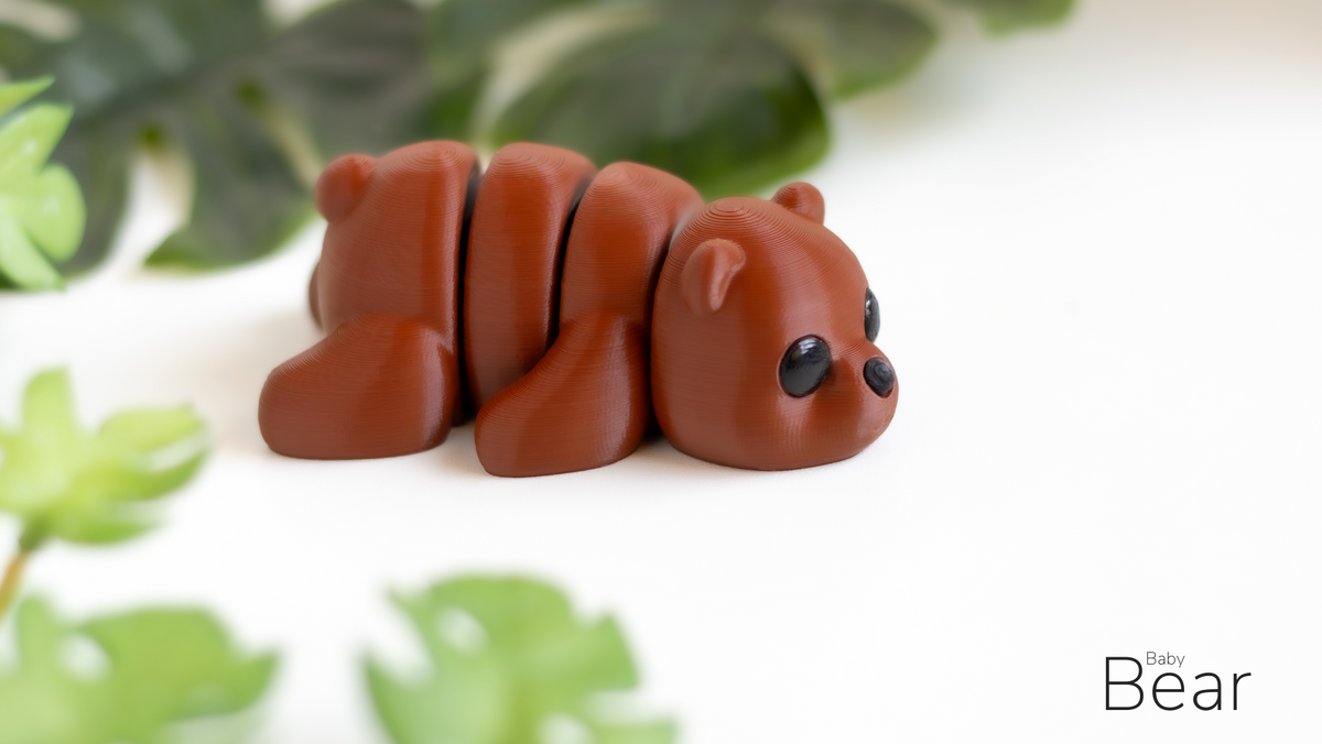 Small brown bear figurine on a white surface with green leaves in the background