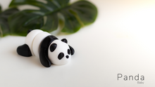 Panda-shaped object on a white surface with green leaves in the background