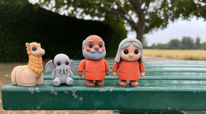 Four articulated fidgets a woman, man, Cthulhu and an alpaca on a green bench with a natural background