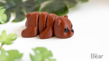 Small brown bear figurine on a white surface with green leaves in the background