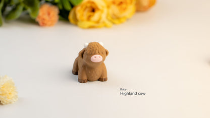 Small brown Highland cow figurine on a white surface with flowers in the background