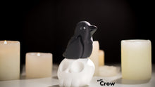 Black crow figurine on a white pedestal with candles in the background