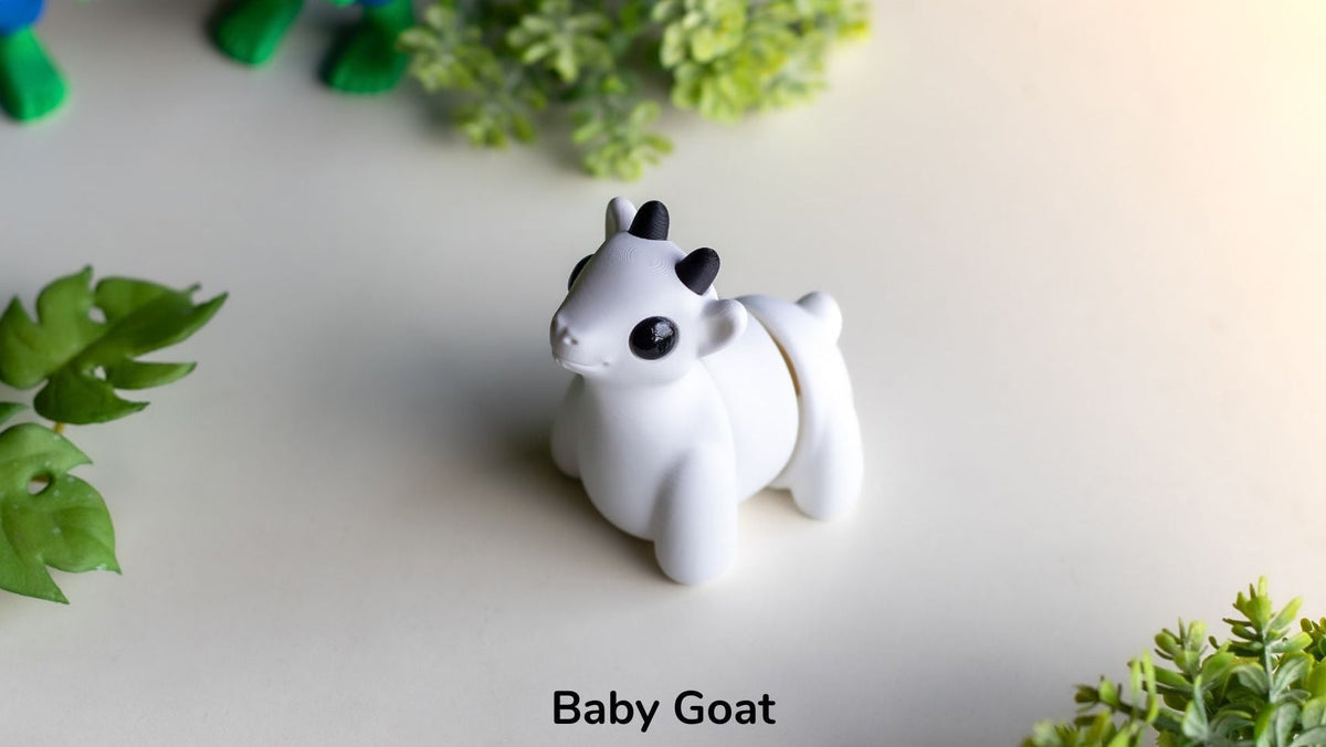 White goat figurine labeled 'Baby Goat' on a light surface with green leaves.