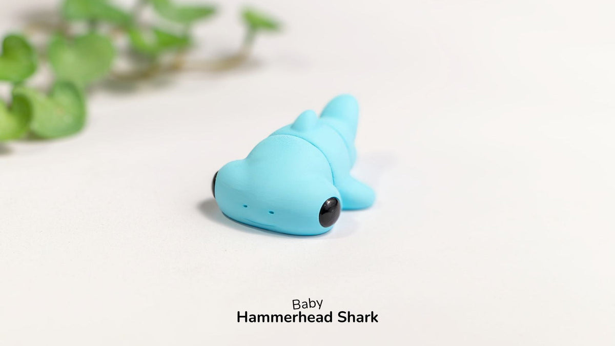 Blue toy hammerhead shark on a white surface with green leaves in the background