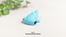 Blue toy hammerhead shark on a white surface with green leaves in the background