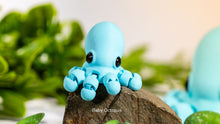 Blue octopus figurine on a rock with green plants in the background