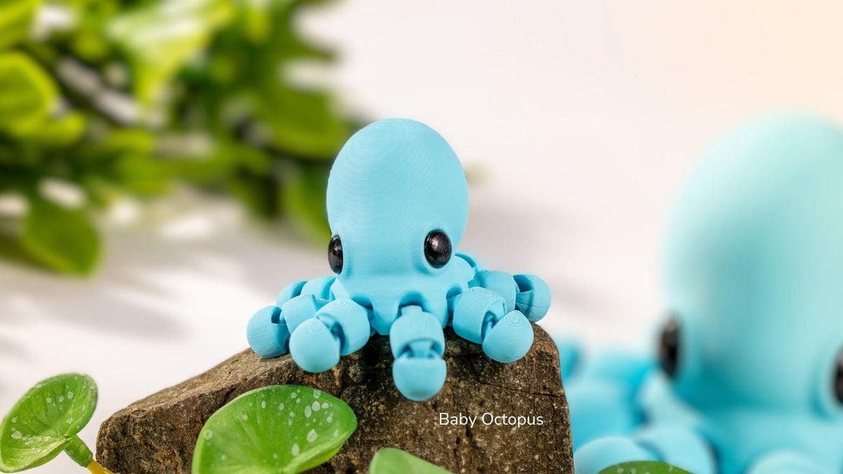 Two small blue octopus figurines on a rock with green leaves.