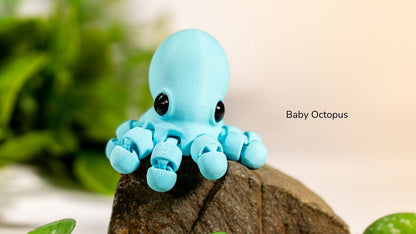 Blue baby octopus toy on a rock with green plants in the background