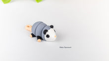 Grey and white Baby Opossum fidget toy on a white surface
