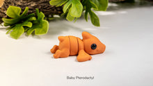 Baby pterodactyl figurine on a white surface with green leaves in the background