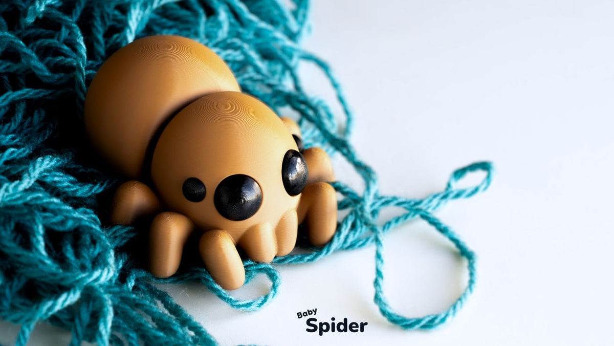 A small tan spider-shaped toy with large black eyes resting on a pile of teal yarn against a white background. The text 'toy Spider' appears near the bottom right.