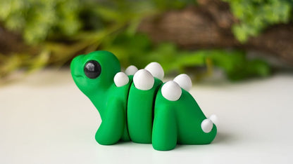 Green baby stegosaurus toy figure on a white surface with blurred greenery in the background