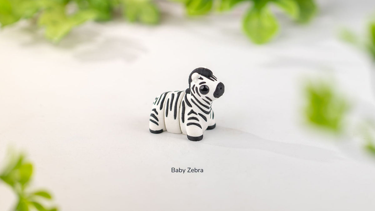 Toy zebra figurine on a white surface with green leaves in the background