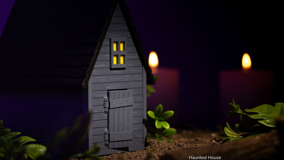 Haunted House model lit up beside candles at night