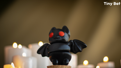 Small black bat figurine with red eyes on a cork base, surrounded by candles.
