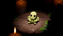 Small green creature figurine on a dark surface with candles around