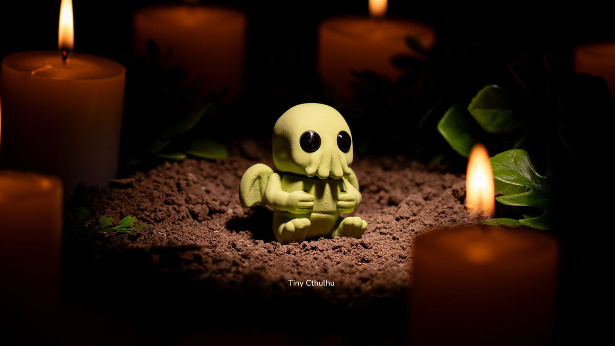 Green Tiny Cthulhu figure lit by candles on a dark background
