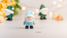Small gnome figurine with a blue hat and outfit on a light background with blurred decorative elements.