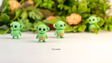 Three green Tiny Goblin fidget toys with flowers behind