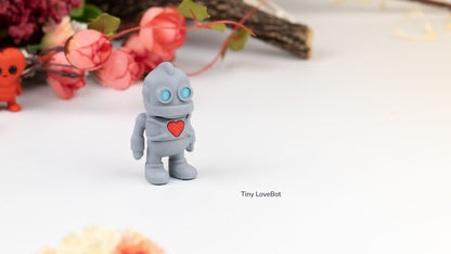 Grey Tiny Lovebot robot holding a red heart, with flowers behind